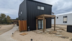 A modern building with a black exterior, a wooden pergola, and a paved walkway leading to a wooden gate. - Family Friendly Lake Front New Build - 5bdrm + Hot Tub (Stevensville)