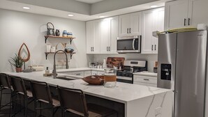 A modern kitchen with white cabinets, a large island with bar stools, a stainless steel refrigerator, and a microwave. - Family Friendly Lake Front New Build - 5bdrm + Hot Tub (Stevensville)