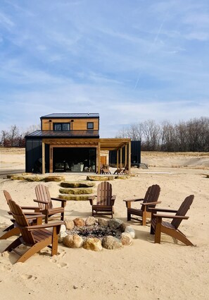 A modern house with a large open porch, a fire pit, and several Adirondack chairs. - Family Friendly Lake Front New Build - 5bdrm + Hot Tub (Stevensville)