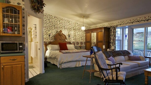 A cozy bedroom with a bed, a rocking chair, a sofa, and a wooden cabinet. - Private Cottage “Wild Rose” (Julian)