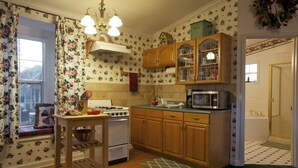 A kitchen with wooden cabinets, a stove, a microwave, and a window with floral curtains. - Private Cottage “Wild Rose” (Julian)