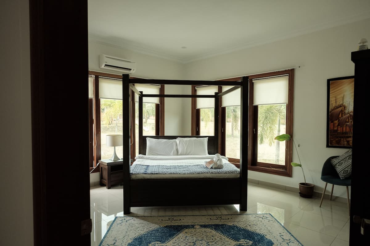 A four-poster bed with a white and blue bedspread, a bedside table with a lamp, and a potted plant.