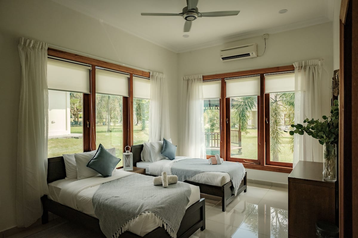 A hotel room with two beds, large windows, a ceiling fan, and a potted plant.