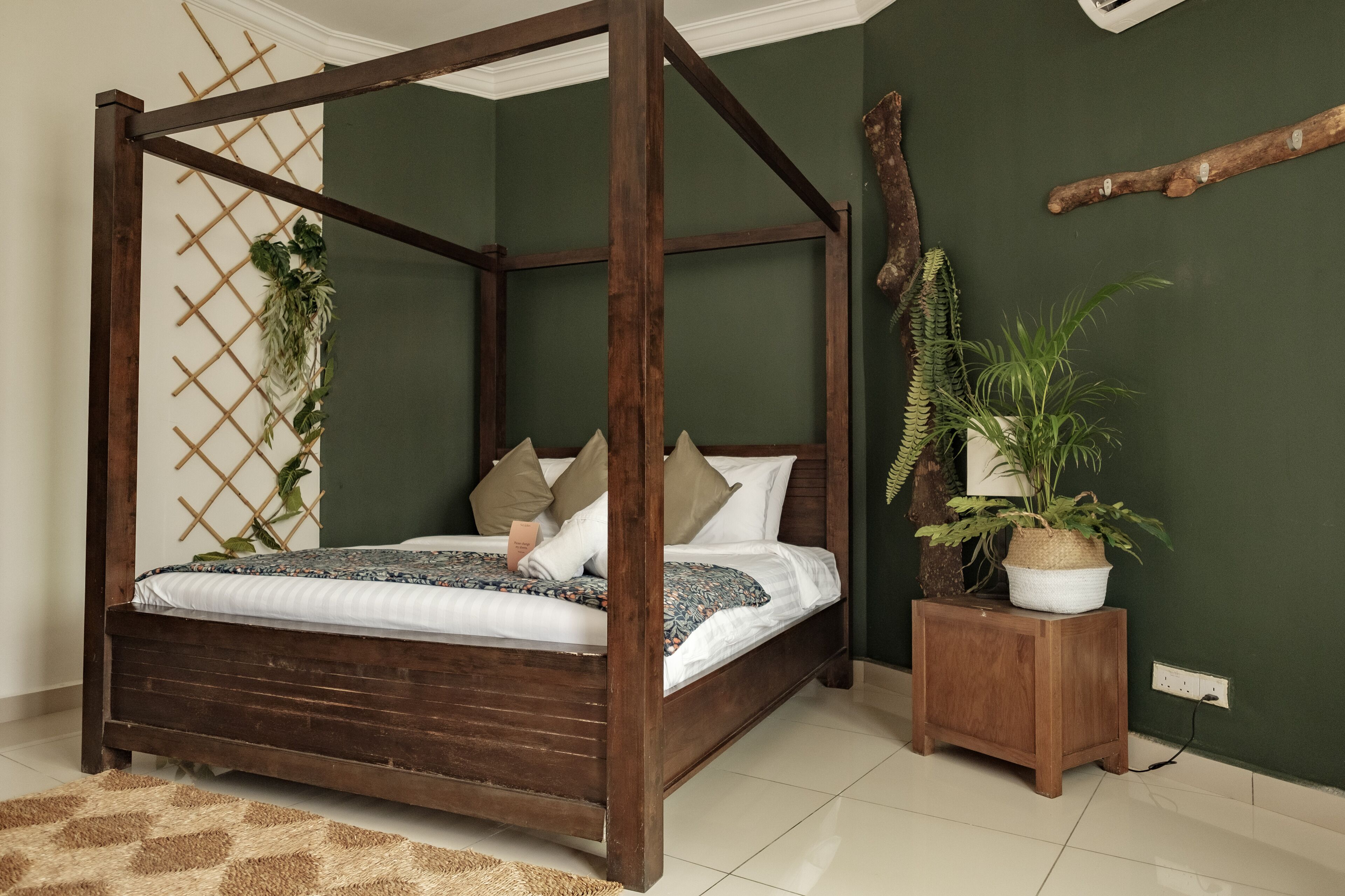 Un letto a baldacchino con struttura in legno, una parete verde e un comodino in legno con una pianta.