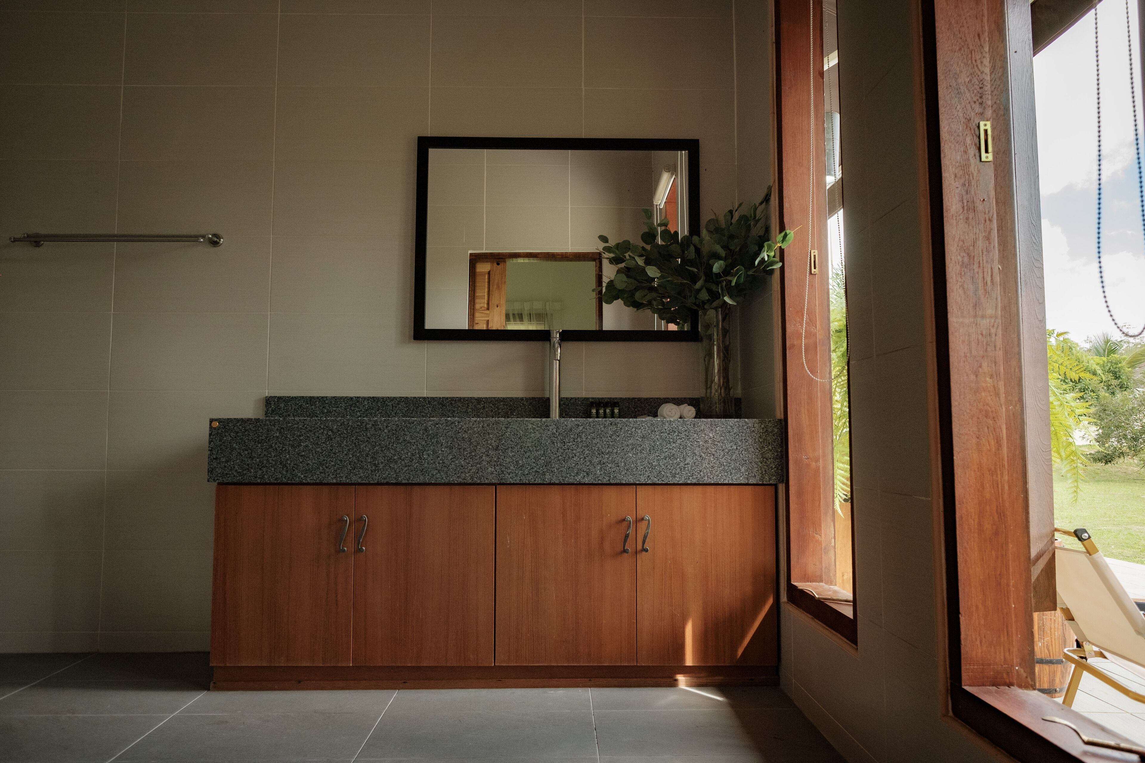 A bathroom with a wooden vanity, a mirror, and a window with a view of greenery.