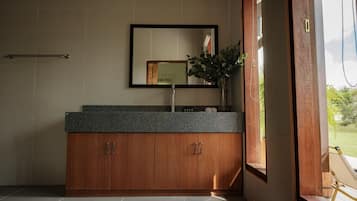 A bathroom with a wooden vanity, a mirror, and a window with a view of greenery.