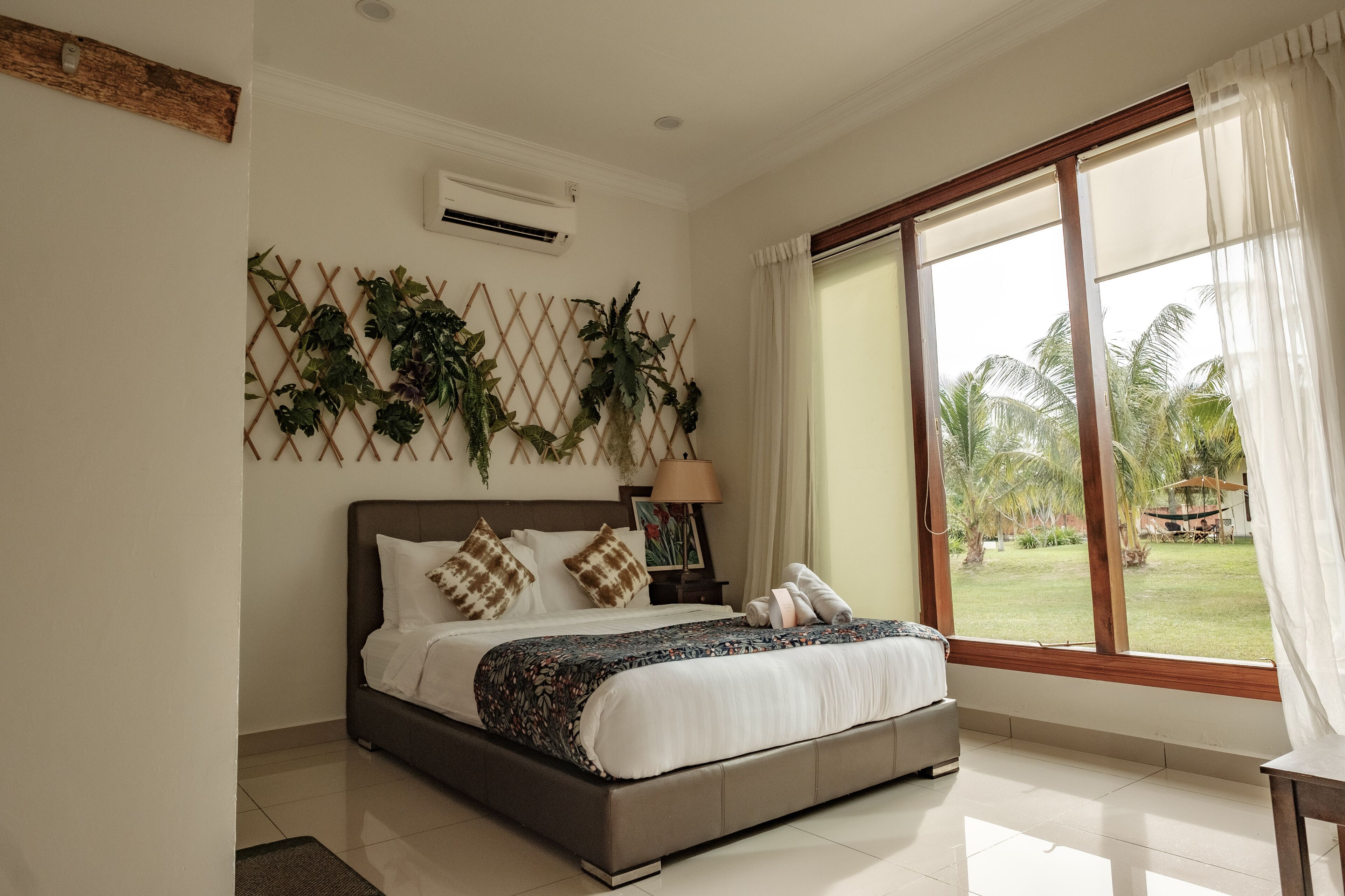 A bedroom with a bed, a window with curtains, a wall-mounted air conditioner, and a decorative plant wall.