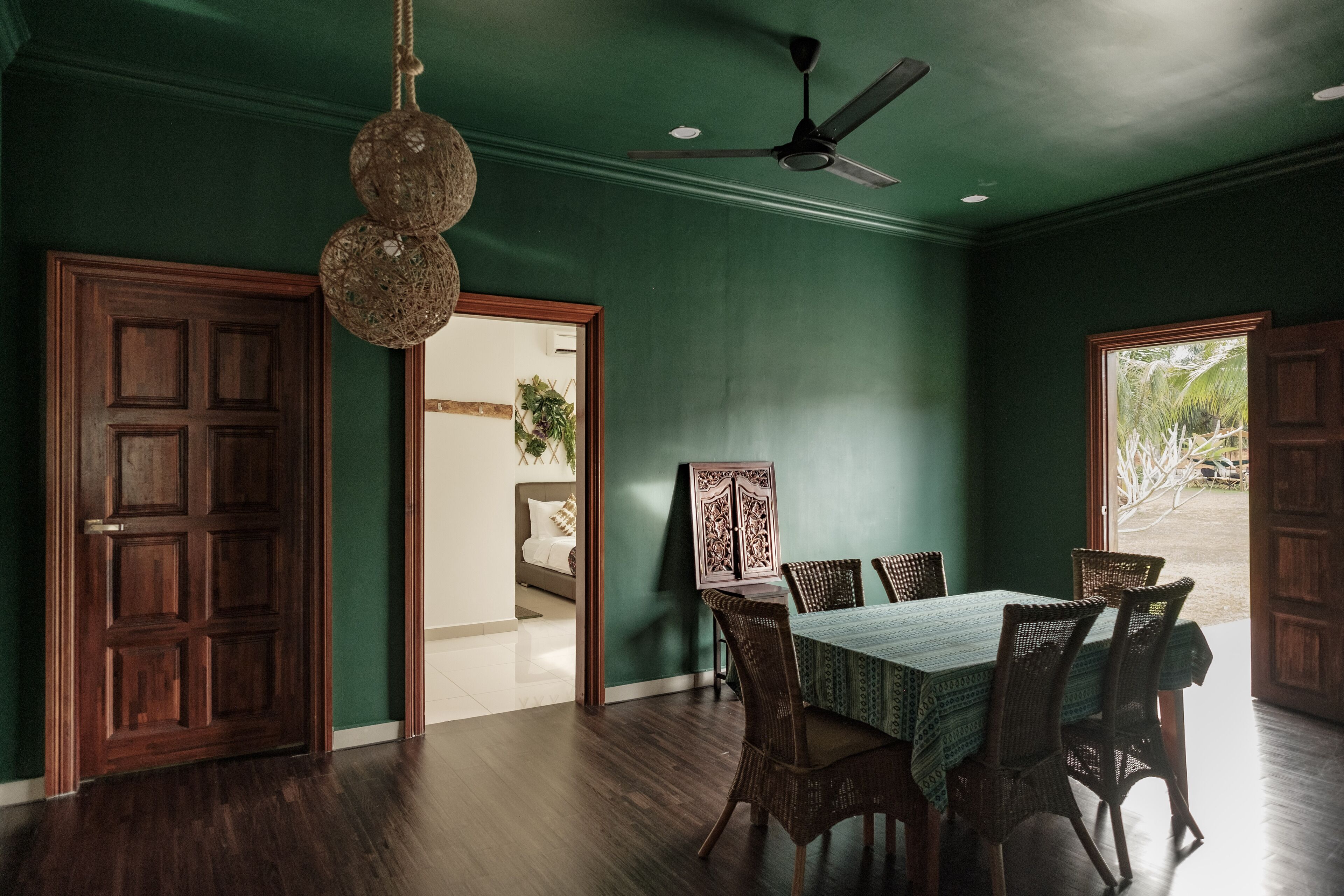 A dining area with a table set for four, surrounded by wicker chairs, a ceiling fan, and a hanging light fixture.