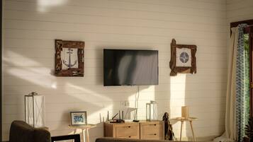 A living room with a flat-screen TV mounted on the wall, wooden furniture, and a window with patterned curtains.