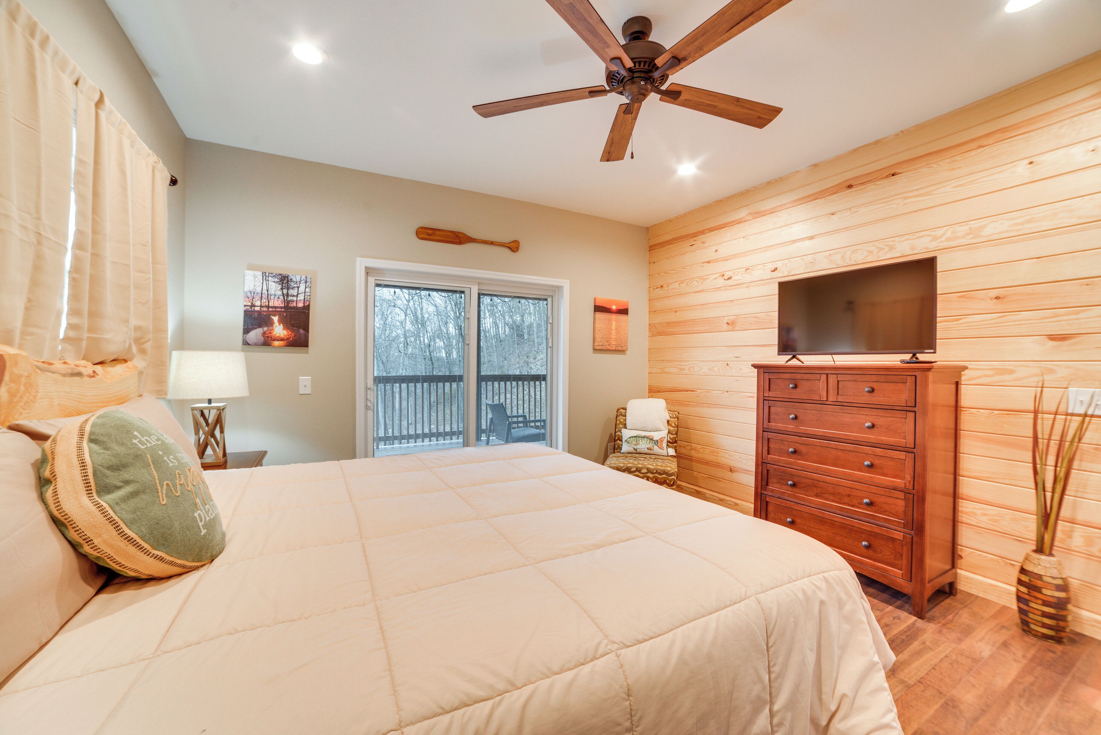 A bedroom with a bed, a dresser, a television, and a ceiling fan.