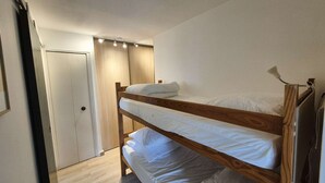 A bunk bed room with a wooden headboard, white bedding, and a door with a light switch. - Renovated studio close to the beach of Sainte Asile in Pin Rolland (ST MANDRIER SUR MER)