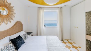 Een slaapkamer met een bed, een raam met uitzicht op zee, een plafond met een geel ontwerp en een muur met een decoratief paneel.