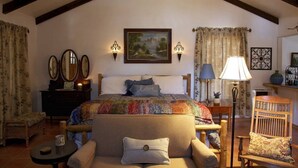 A cozy bedroom with a large bed, a wooden chair, a small table, and a lamp. - Private Cottage “Storybook Barn” (Julian)