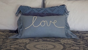 A bed with a patterned bedspread and two pillows, one with the word "love" embroidered on it. - Private Cottage “Storybook Barn” (Julian)