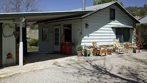 A single-story house with a covered porch, a chimney, and a small garden area with potted plants and outdoor furniture. - Private Cottage “Storybook Barn” (Julian)