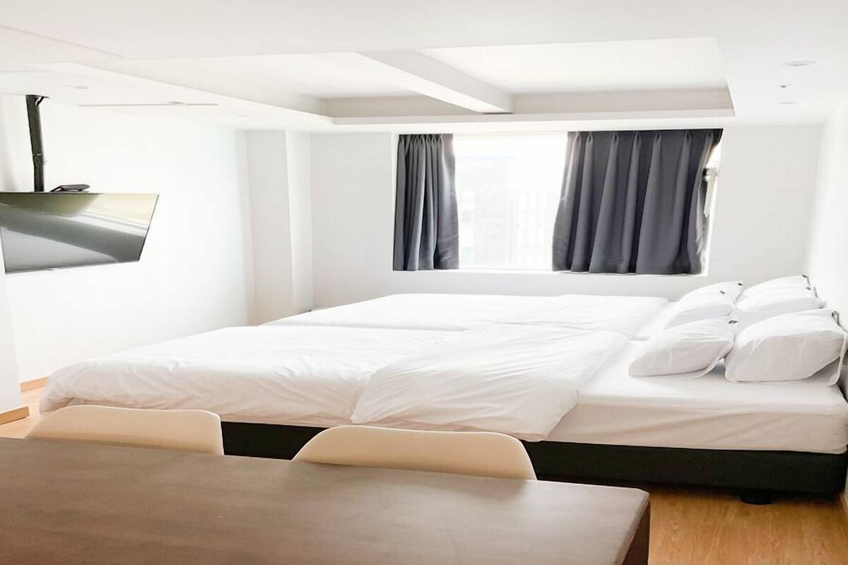 A modern hotel room with a large bed, a flat-screen TV mounted on the wall, and a window with curtains.
