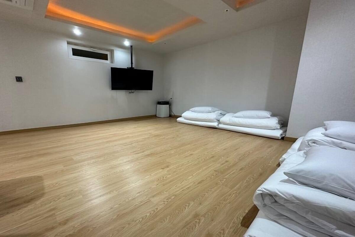 A hotel room with a wooden floor, a flat-screen TV mounted on the wall, and neatly folded white bedding.