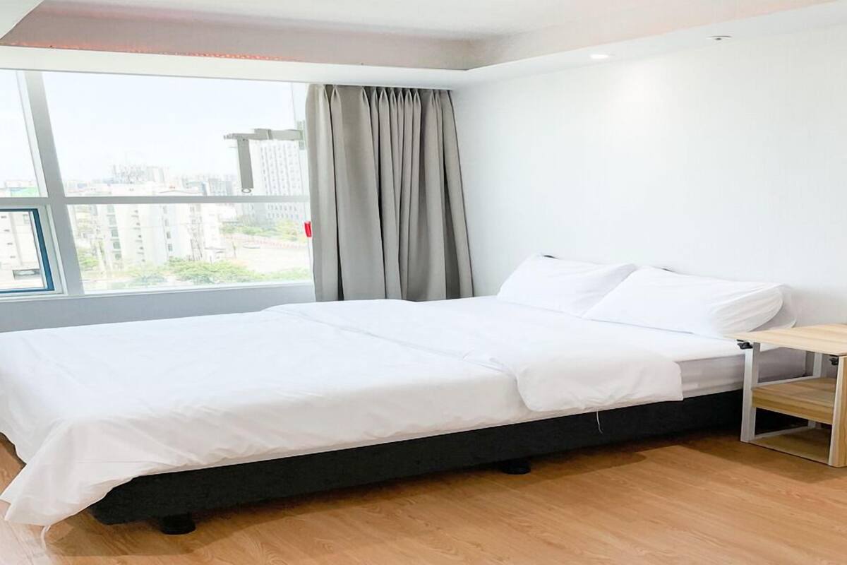 A modern hotel room with a large bed, a bedside table, and a view of the city through the window.
