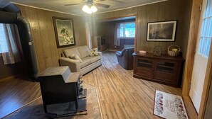 A room with a ceiling fan, wooden walls, a sofa, a dining table, and a cabinet.