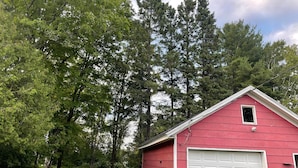 A red shed with a white garage door, surrounded by green trees and a stone wall.