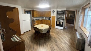 A compact kitchen with wooden cabinets, a white refrigerator, a microwave, and a dining area with a table and chairs.
