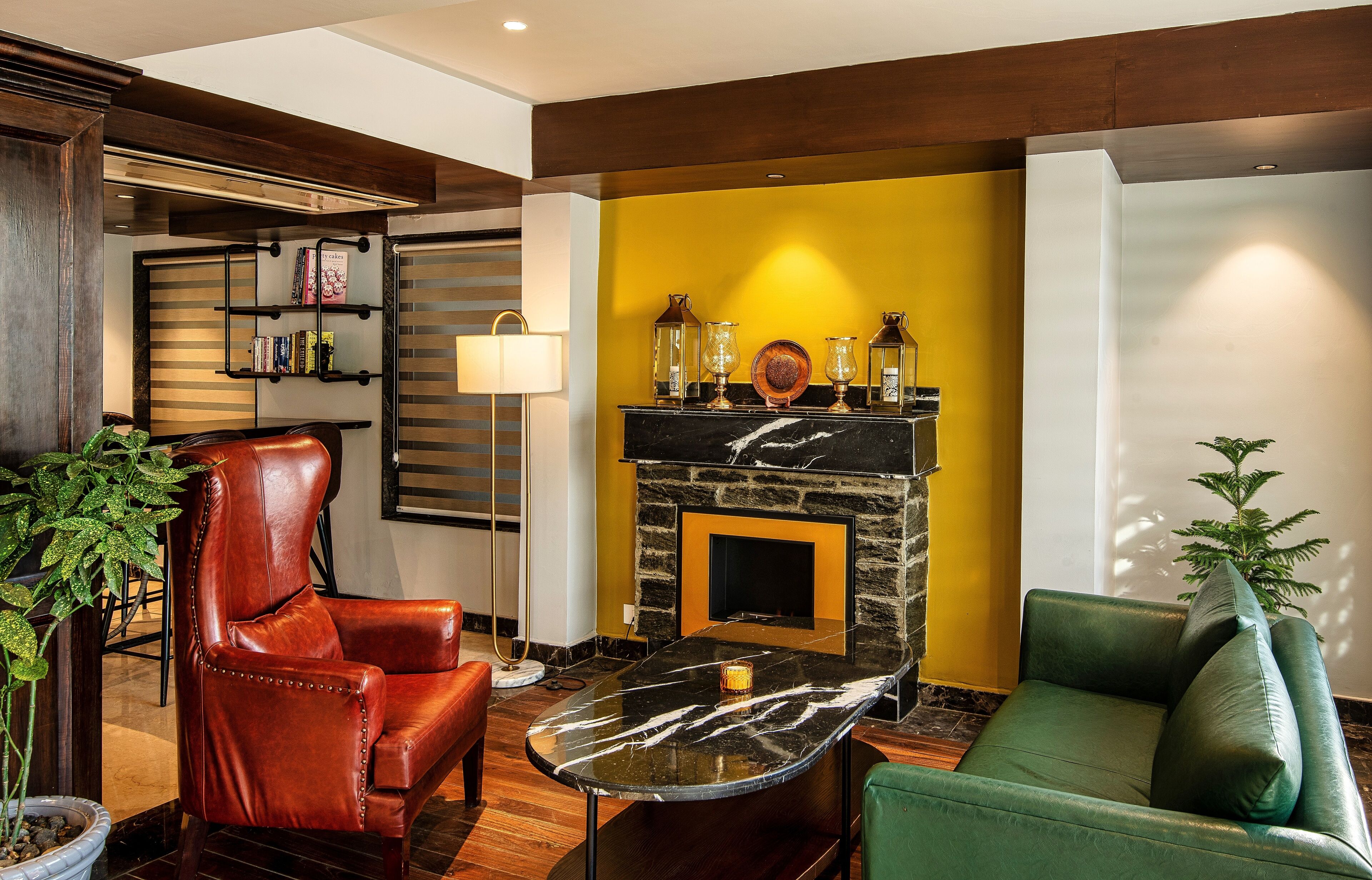 A living room with a leather armchair, a green sofa, a marble coffee table, a fireplace with decorative items, and a bookshelf.
