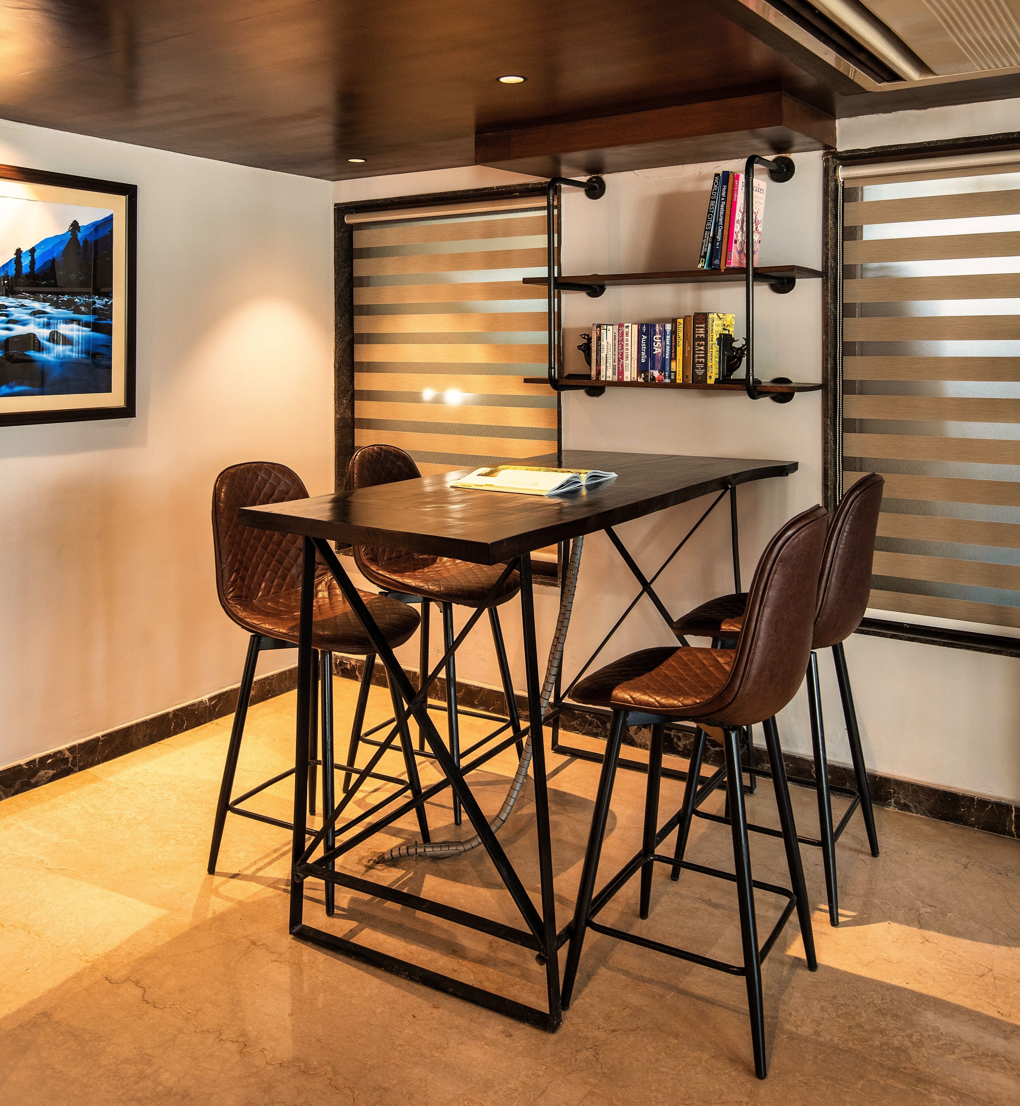 A dining area with a table and four chairs, a bookshelf with books, and a framed picture on the wall.