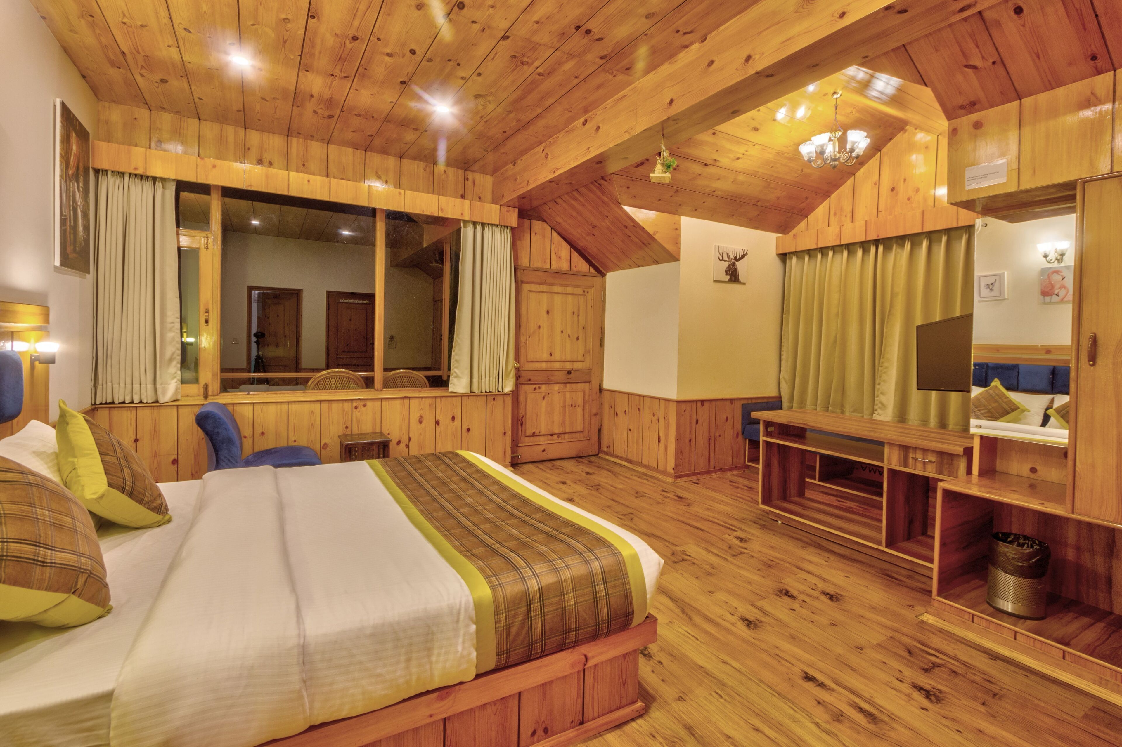 A wooden-floored bedroom with a bed, a desk, and a mirror.