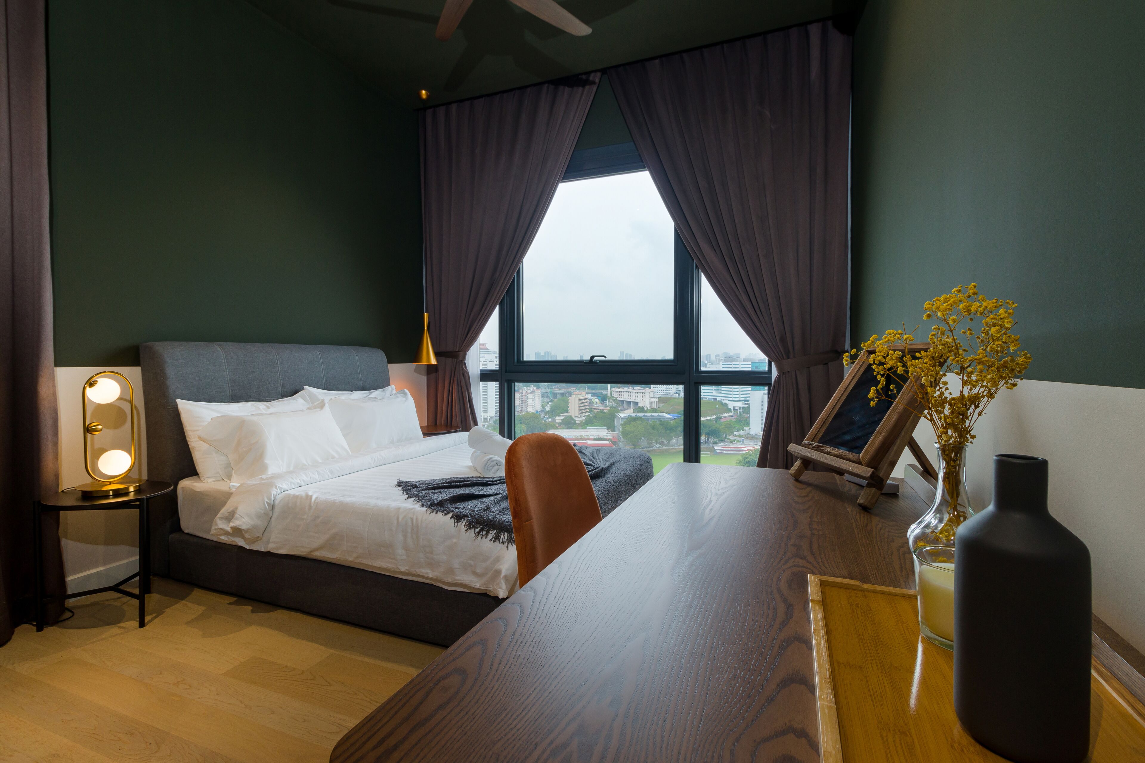 Ein Schlafzimmer mit Bett, Nachttisch, Lampe und Blick auf die Stadt durch große Fenster.