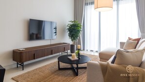Ein modernes Wohnzimmer mit Flachbildfernseher, rundem Couchtisch mit Kerzen, einer Topfpflanze und einer Couch.
