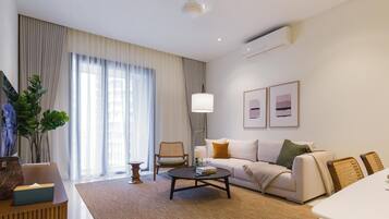 A modern living room with a sofa, coffee table, and chairs. There is a TV, a plant, and a lamp.