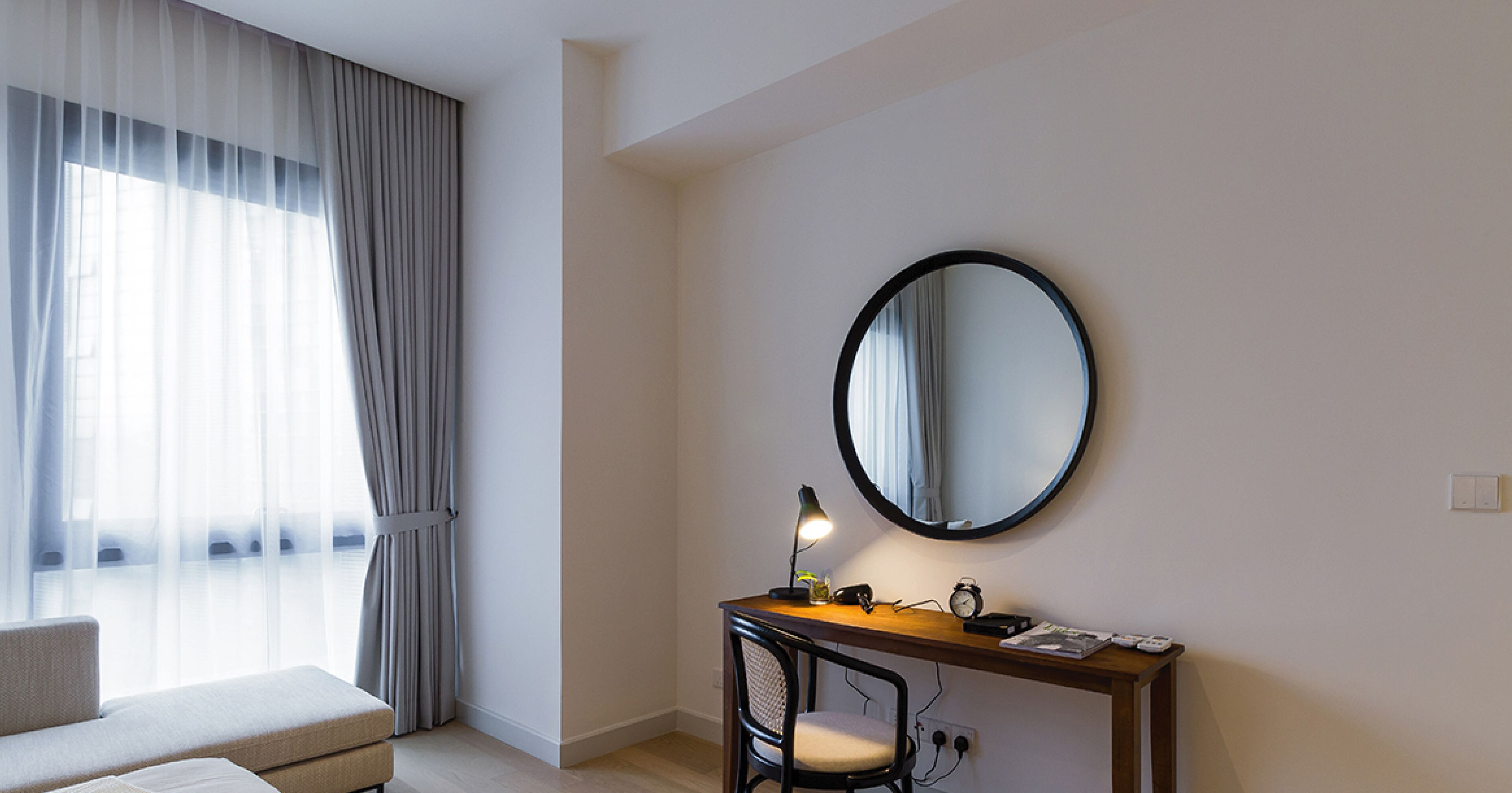 A hotel room with a desk, chair, and a round mirror on the wall.