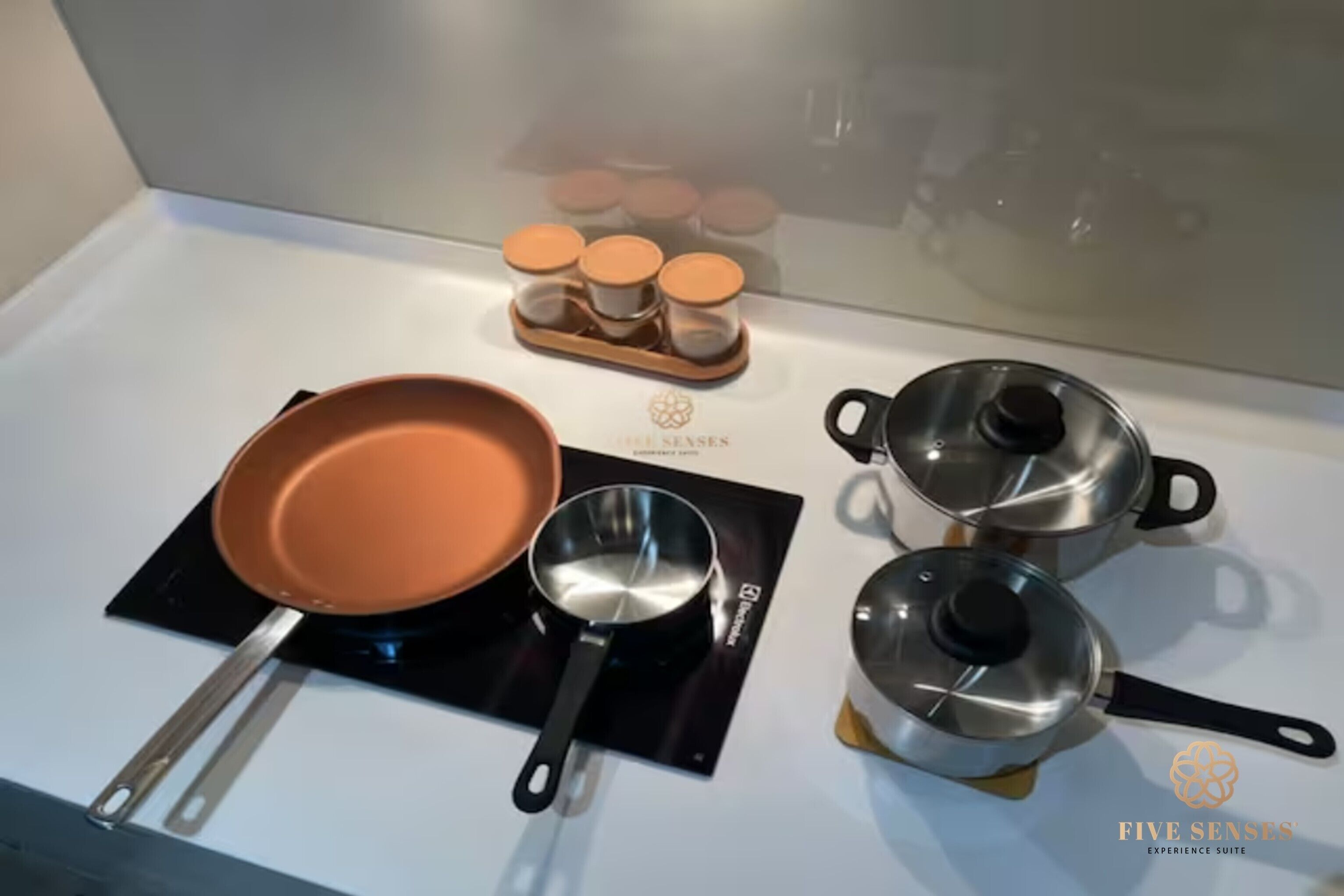 Una cucina con un fornello, una padella, una pentola, un tegame e una spezieria.