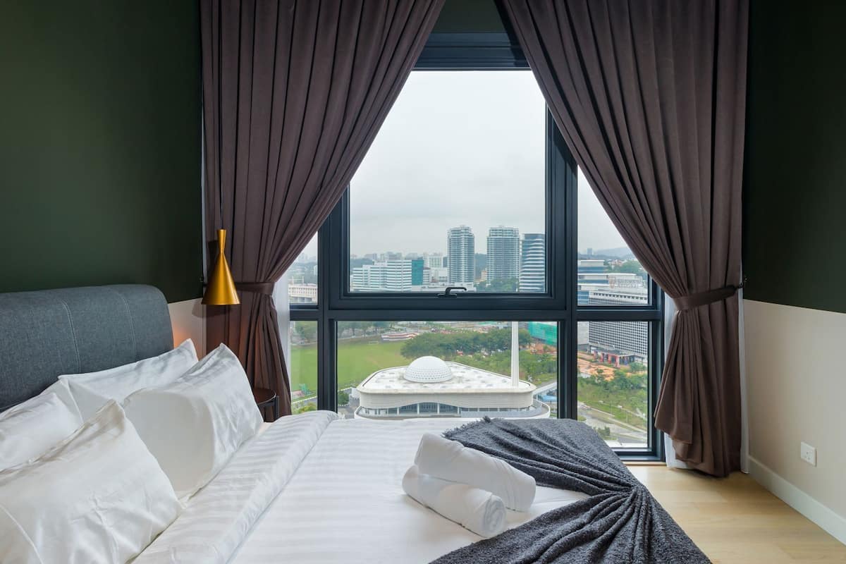 Quarto de hotel com uma janela grande, uma cama e vista para a paisagem urbana.