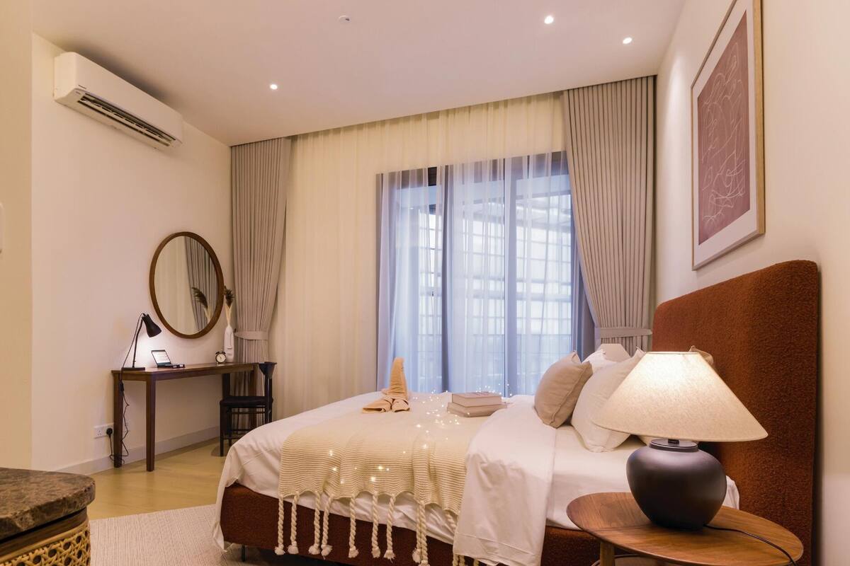 Quarto de hotel moderno com cama, luminária de cabeceira, escrivaninha e ar condicionado.