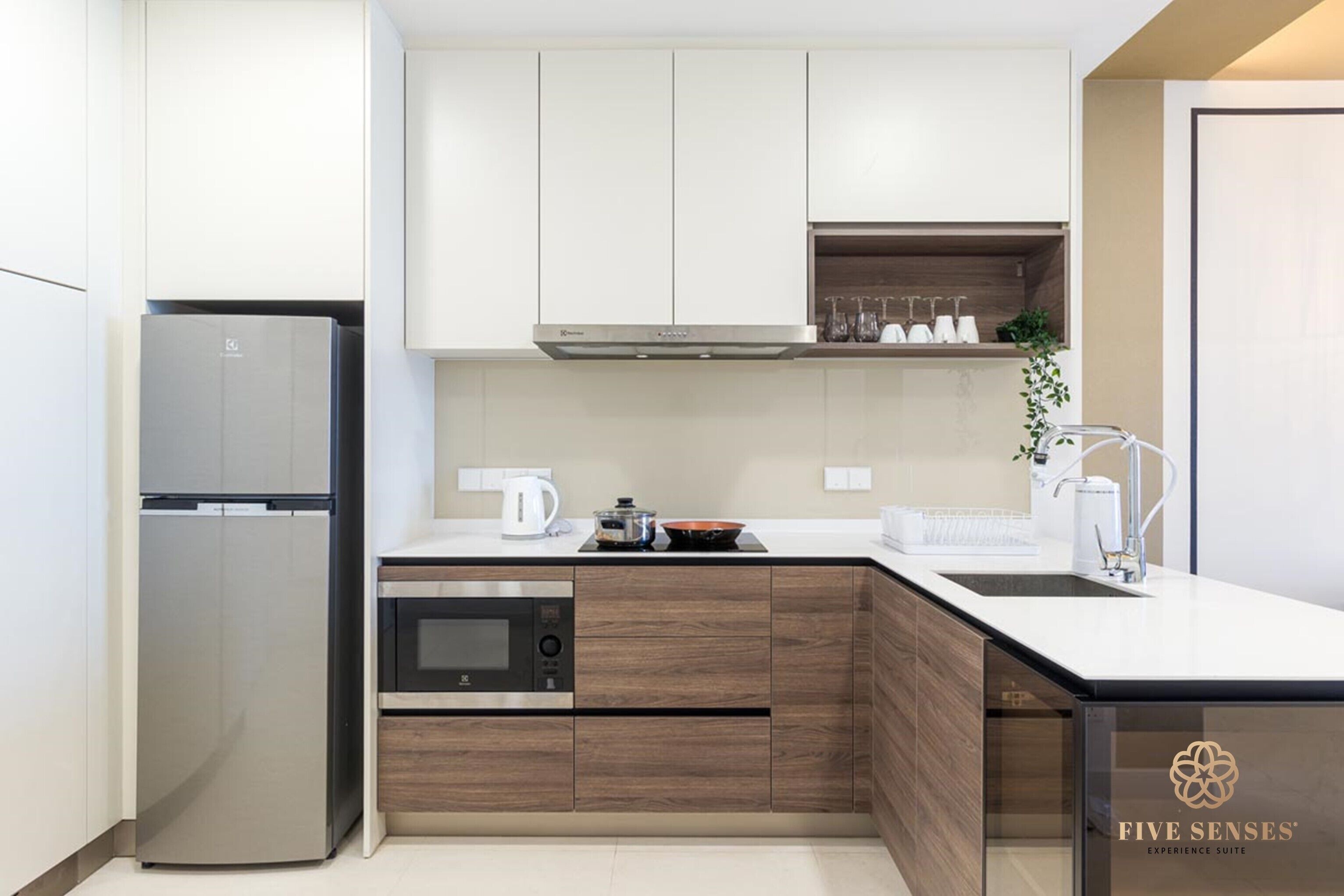Una cocina moderna con un refrigerador de acero inoxidable, horno empotrado y microondas. Hay una encimera de madera con un fregadero y una cafetera.