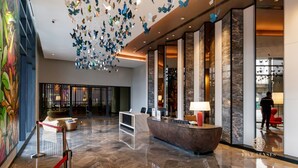 Eine moderne Hotelhalle mit einer Rezeption, einer Sitzecke und einer Decke, die mit Schmetterlingsdekorationen versehen ist.