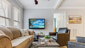Un salon avec un canapé beige, une table basse ornée d’une plante et un téléviseur à écran plat fixé au mur.