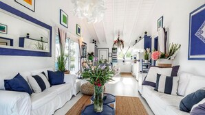 A modern living room with white sofas, blue cushions, and a central coffee table. - Myrtle Cottage - Charming 2 bed Cottage (Paxos)