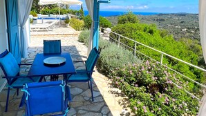 An outdoor patio with a table and chairs, a white umbrella, and a view of the sea. - Myrtle Cottage - Charming 2 bed Cottage (Paxos)