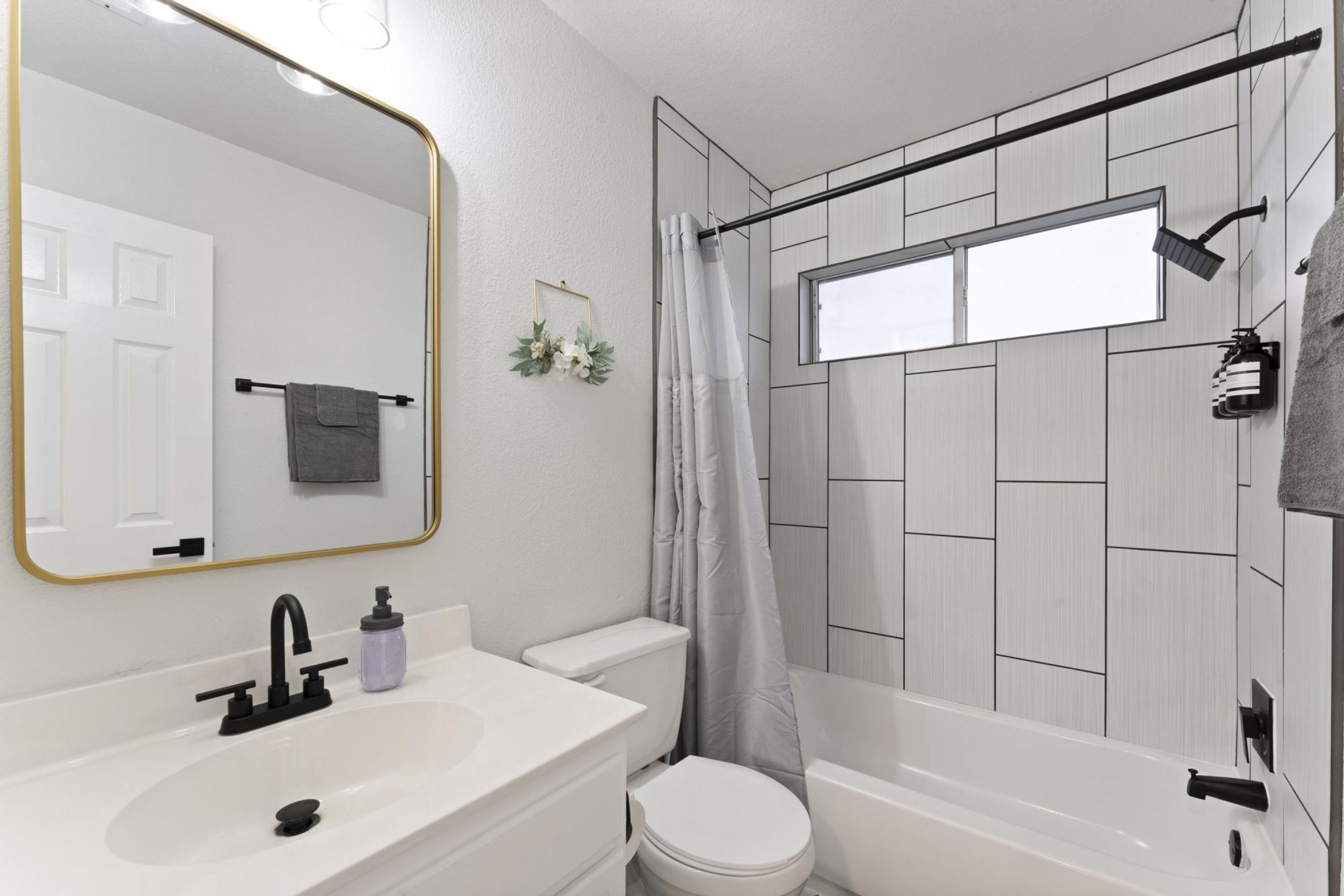 Een moderne badkamer met een wit wastafel, een zwarte kraan, een wit toilet en een douche met een grijs gordijn.