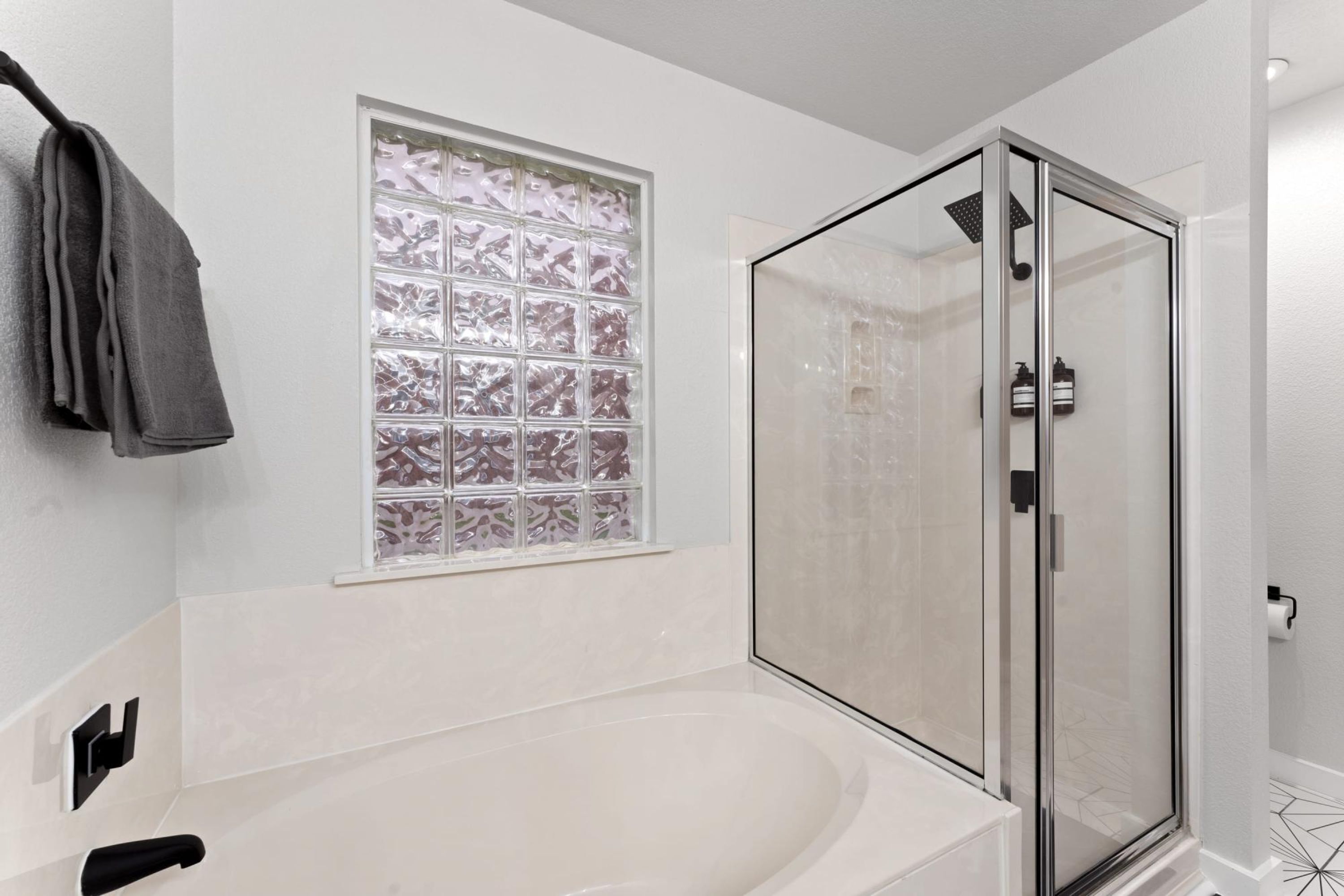 A modern bathroom with a glass-enclosed shower, a large bathtub, and a frosted window.