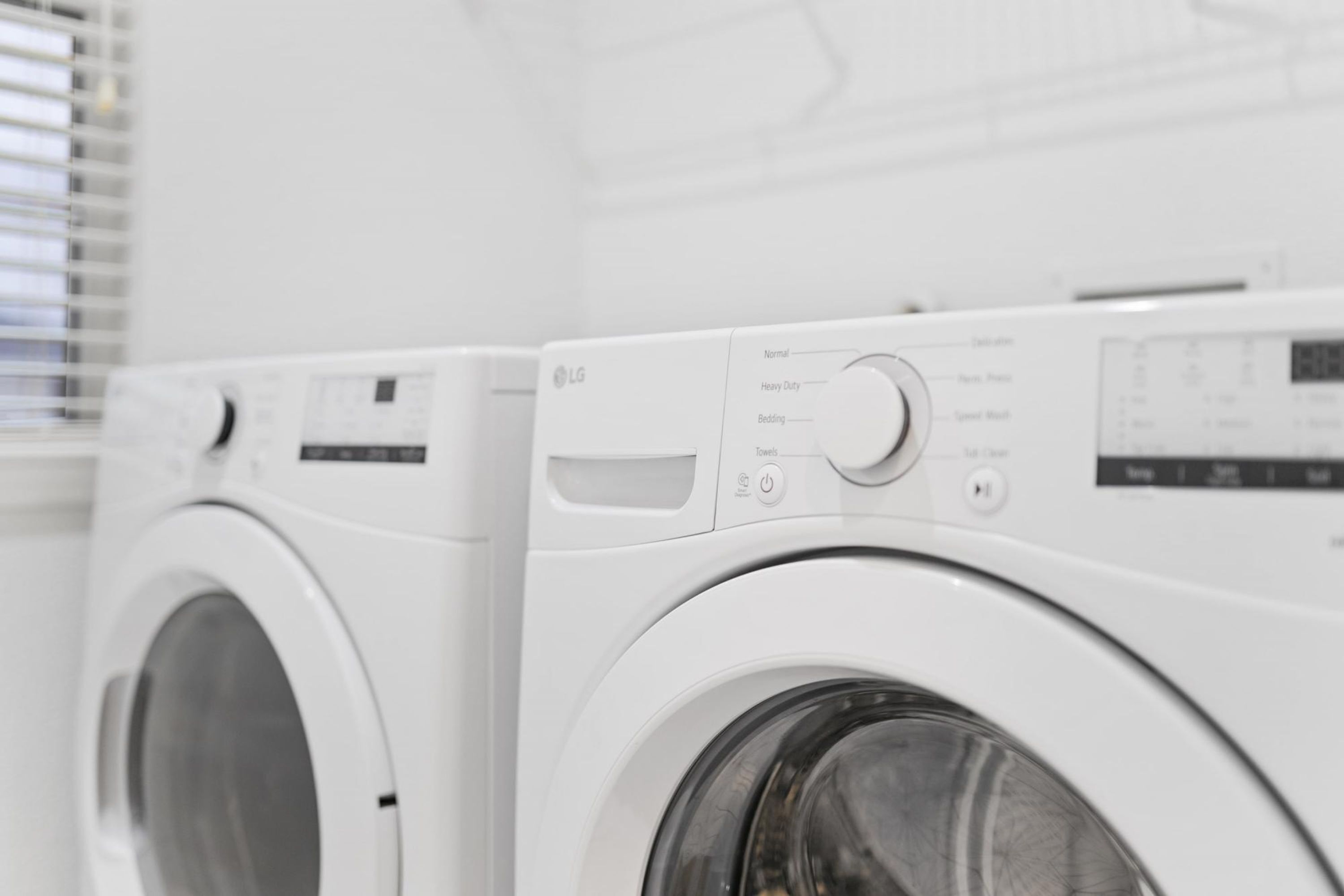 A row of white washing machines in a room with a window and a white wall.