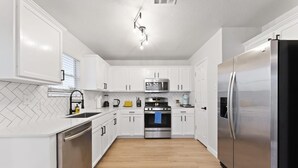 A modern kitchen with white cabinets, a stainless steel refrigerator, a microwave, and a dishwasher.