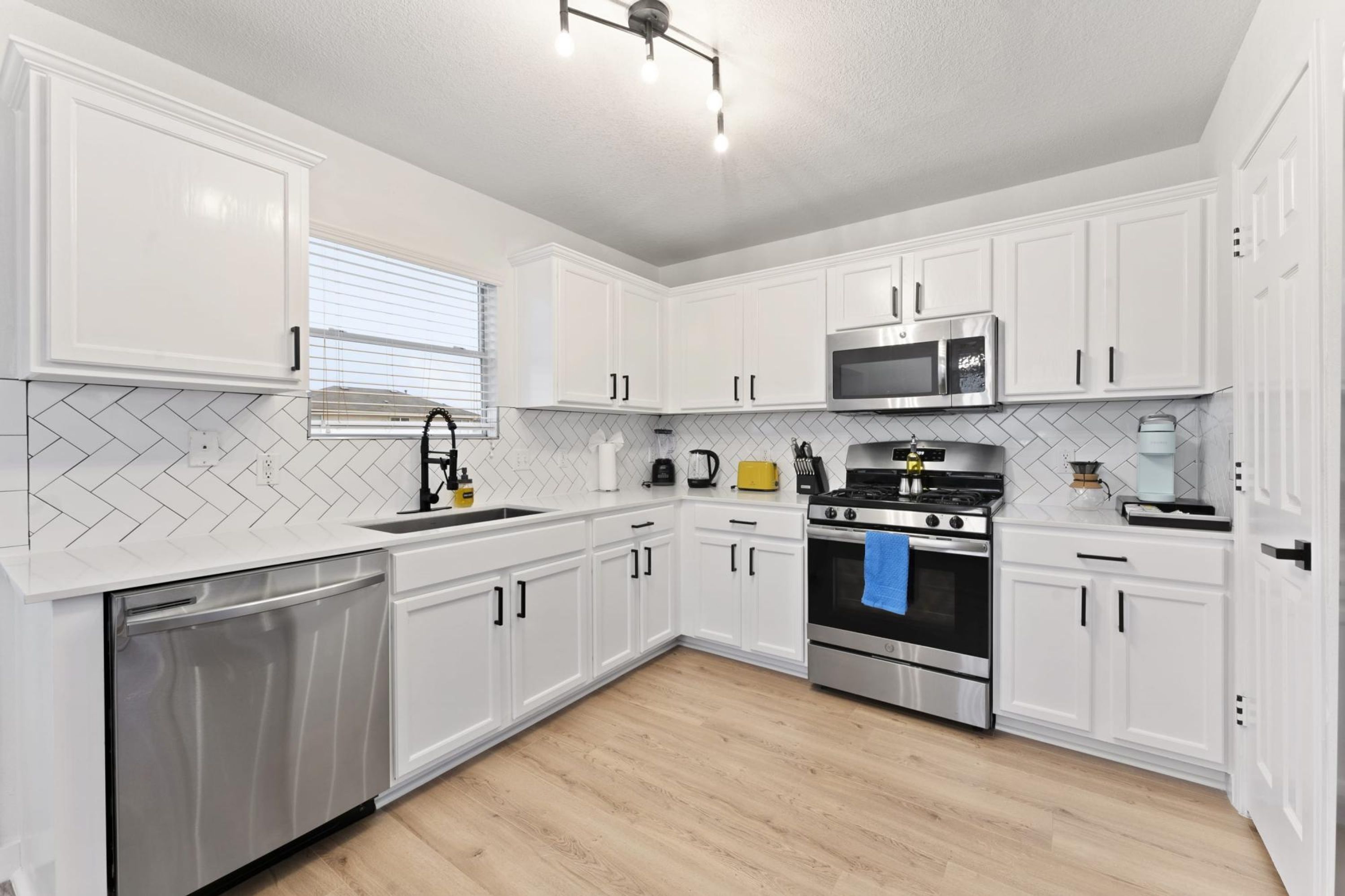 A modern kitchen with white cabinetry, a stainless steel dishwasher, a double oven, and a microwave.
