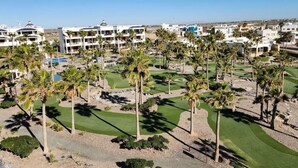 Ett semesterområde med flera vita byggnader, en golfbana och palmer.