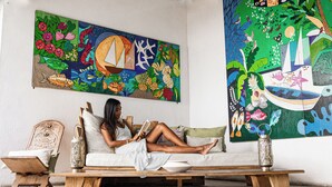 Una mujer leyendo en un sofá con un mural colorido de fondo.