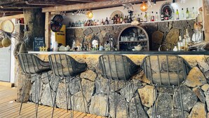 Zona de bar con paredes de piedra, sillas de mimbre y una variedad de botellas y vasos.