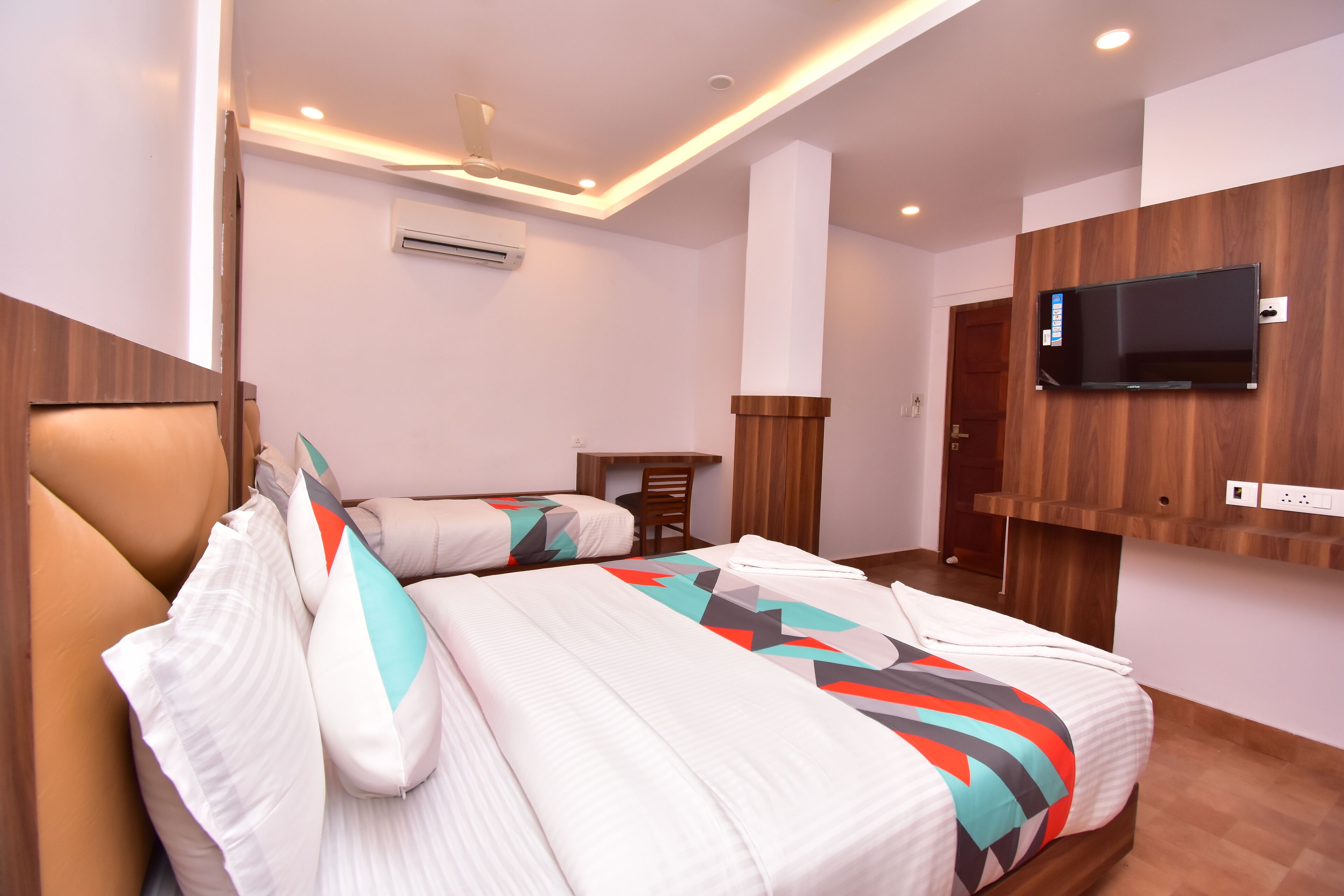 A hotel room with two beds, a TV mounted on the wall, and an air conditioning unit.