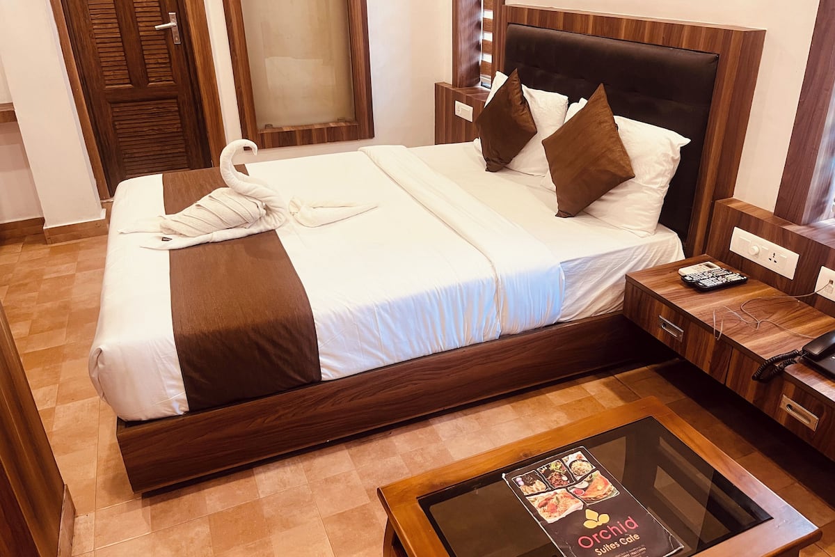 Una cama bien hecha con un cabecero marrón, una mesita de noche con control remoto y una mesa de vidrio con un menú.